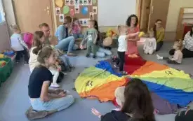 pani nauczycielka wraz z dziećmi i rodzicami siedzą dokoła chusty animacyjnej dzieci oglądają zabawki