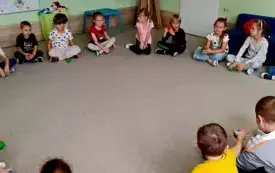 dzieci siedzą w kole na dywanie przed nimi leżą kolorowe piłeczki