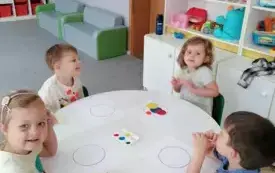 dzieci siedzą przy okrągłym stoliku i stemplują farbami szablony k&oacute;ł