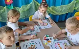 dzieci siedzą przy stoliku i wykonują pracę plastyczną z użyciem farb paluszkami stemplują kropkę