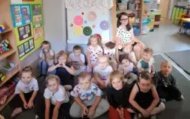 grupa dzieci siedzi na dywanie pozują do zdjęcia grupowego wraz z panią w tle dekoracja dzień kropki
