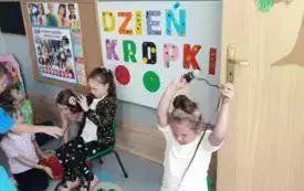 dwie dziewczynki siedzą na krzesełkach i nawijają wstążkę widać inne dzieci w tle dekoracja dzień kropki