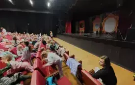 dzieci siedzą na czerwonych fotelach w sali teatralnej widać dekoracje na scenie i panie nauczycielki