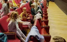 dzieci siedzą na czerwonych fotelach w sali teatralnej