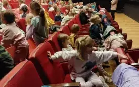 dzieci siedzą na czerwonych fotelach w sali teatralnej