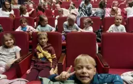 dzieci siedzą na czerwonych fotelach w sali teatralnej