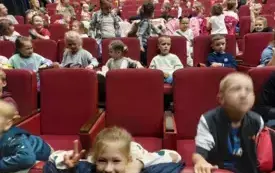 dzieci siedzą na czerwonych fotelach w sali teatralnej