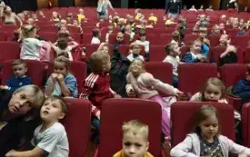 dzieci siedzą na czerwonych fotelach w sali teatralnej