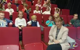 dzieci siedzą na sali teatralnej na czerwonych fotelach przed nimi siedzi pani nauczycielka