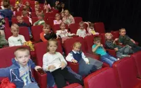 dzieci siedzą na sali teatralnej na czerwonych fotelach 