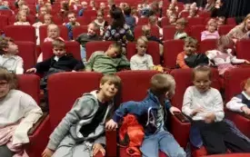 dzieci siedzą na sali teatralnej na czerwonych fotelach 