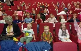 dzieci siedzą na sali teatralnej na czerwonych fotelach