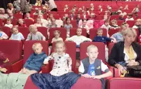 dzieci siedzą na sali teatralnej na czerwonych fotelach