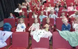 dzieci siedzą na sali teatralnej na czerwonych fotelach