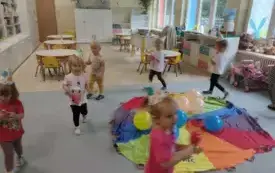 dzieci wok&oacute;ł chusty animacyjnej położonej na podłodze na niej balony