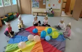 dzieci w kolorowych czapeczkach siedzą przed chusta animacyjna, na chuście leżą kolorowe balony