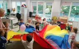 dzieci wsp&oacute;lnie z panią trzymają chustę animacyjną na kt&oacute;rej są balony