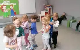 dzieci idą w rzędzie z rękami na ramionach koleg&oacute;w dw&oacute;ch chłopc&oacute;w w tle siedzi na kanapach