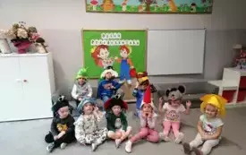 dzieci pozują do zdjęcia na tle dekoracji dzień przedszkolaka dzieci mają na głowach czapki w r&oacute;żnych kształtach kwiatek, biedronka itp
