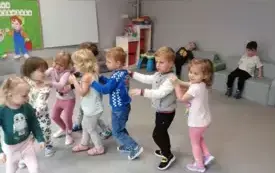 dzieci idą w rzędzie z rękami na ramionach koleg&oacute;w dw&oacute;ch chłopc&oacute;w w tle siedzi na kanapach