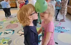 dwie dziewczynki w parze trzymają balon pomiędzy głowami w tle inne dzieci