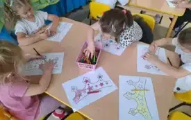 cztery dziewczynki siedzą przy stoliku przed nimi leżą kolorowanki z motywem korony na środku stołu stoją kredki w koszyczku