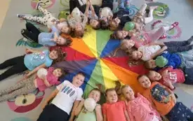 dzieci leżą dookoła na chuście animacyjnej na kt&oacute;rej mają głowy i tworzą koło