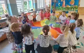 dzieci trzymają dookoła chustę animacyjną na kt&oacute;rej znajdują się balony