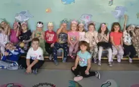 grupa dzieci siedzi na ławce część dzieci na dywanie pozują do zdjęcia grupowego na głowach mają wykonane z papieru własnoręcznie pokolorowane korony