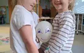 dwie dziewczynki w parze trzymają balonik pomiędzy brzuchami na baloniku namalowana uśmiechnięta buzia