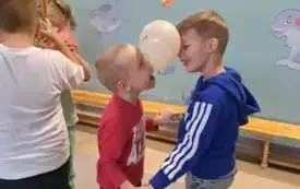 chłopcy w parze trzymają balon pomiędzy głowami widać obok inne dzieci