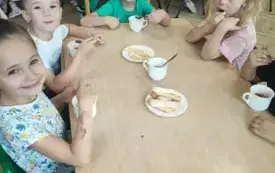 dzieci siedzą przy stolikach przed nimi napełnione filiżanki i talerzyki z ciastkami