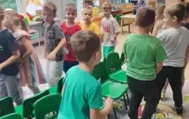 dzieci idą dookoła rzędu krzesełek ustawionych siedziskami do zewnątrz