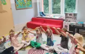 dzieci siedzą w kole na dywanie i trzymają w g&oacute;rze gumę animacyjną
