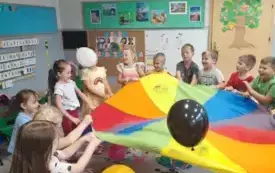 dzieci trzymają dookoła chustę animacyjną na kt&oacute;rej jest kilka balon&oacute;w