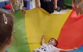 dzieci trzymają dookoła chustę animacyjną na kt&oacute;rej leży chłopiec