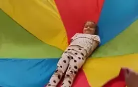 dzieci trzymają dookoła chustę animacyjną na kt&oacute;rej leży dziewczynka