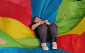 dzieci trzymają dookoła chustę animacyjną na kt&oacute;rej leży jedno dziecko 