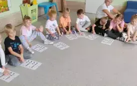 dzieci siedzą w kole przed nimi znajdują się karteczki z kropkami i zygzakami