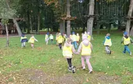 dzieci w kamizelkach odblaskowych biegające po parku