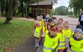 dzieci w kamizelkach odblaskowych stoją w parach na chodniku w parku