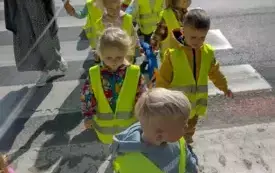 dzieci ubrane w kamizelki odblaskowe wraz z paniami idą przez przejście dla pieszych  trzymając węża spacerowego