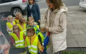 grupa dzieci w kamizelkach odblaskowych stoi wraz z paniami przed skrzynkami wypełnionymi jabłkami