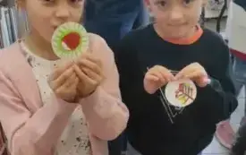 dwie dziewczynki pokazują swoje prace o tematyce jesiennej namalowane na okrągłych karteczkach w tle pani