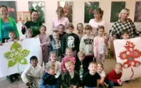 dzieci wraz z paniami pozują do zdjęcia grupowego po obu stronach dzieci trzymają plakaty z liśćmi