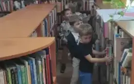 dzieci stoją pomiędzy regałami na kt&oacute;rych stoją książki