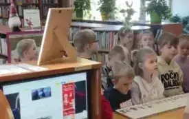 dzieci stoją przed pulpitem w bibliotece w tle regały z książkami