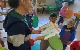 pani trzyma w dłoniach obrazek z namalowanymi wazonami i kwiatami w tle dzieci 