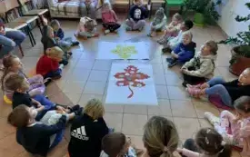 dzieci siedzą w kole na kolorowych okrągłych poduszkach na środku leżą plakaty z dużymi liśćmi ż&oacute;łtym i brązowym