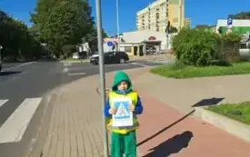 chłopiec stoi pod znakiem drogowym przejście dla pieszych i trzyma obrazek z takim znakiem